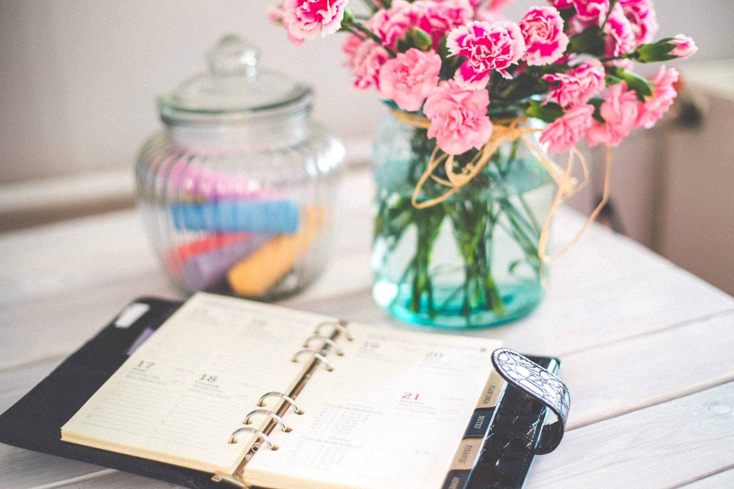 Planner, a vase with flowers, and a candy jar on the white table